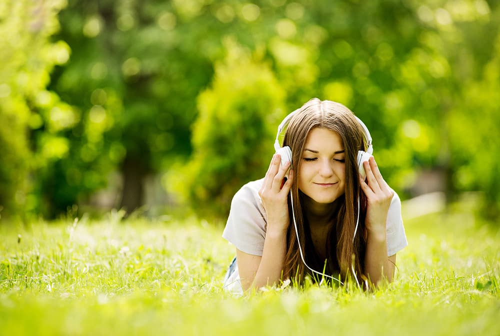 An artiste smiling with headphones on, relaxing in a sunlit meadow